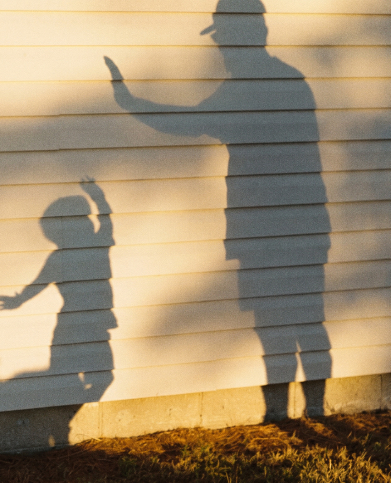 The shadow of a parent and child cast on a sunlit clapboard wall at golden hour